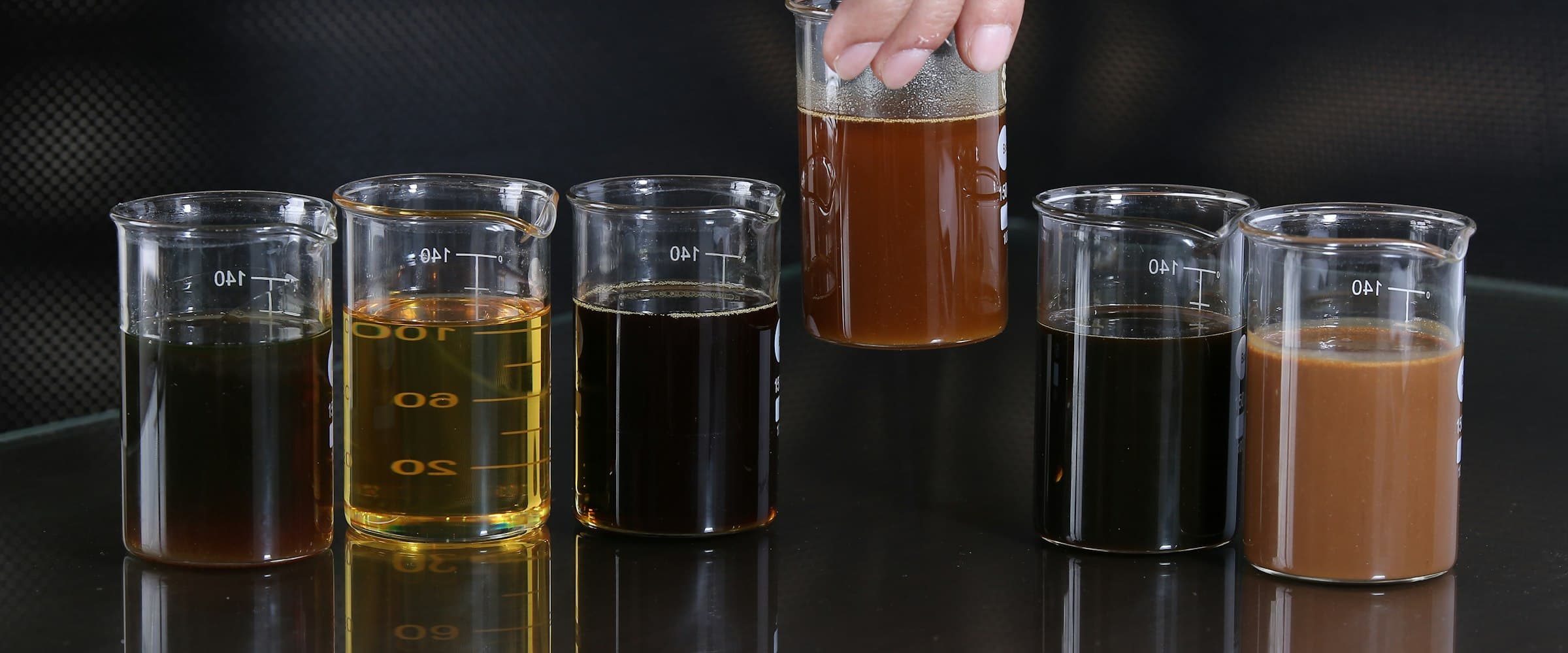 Hand holding a beaker of liquid above several other lab beakers